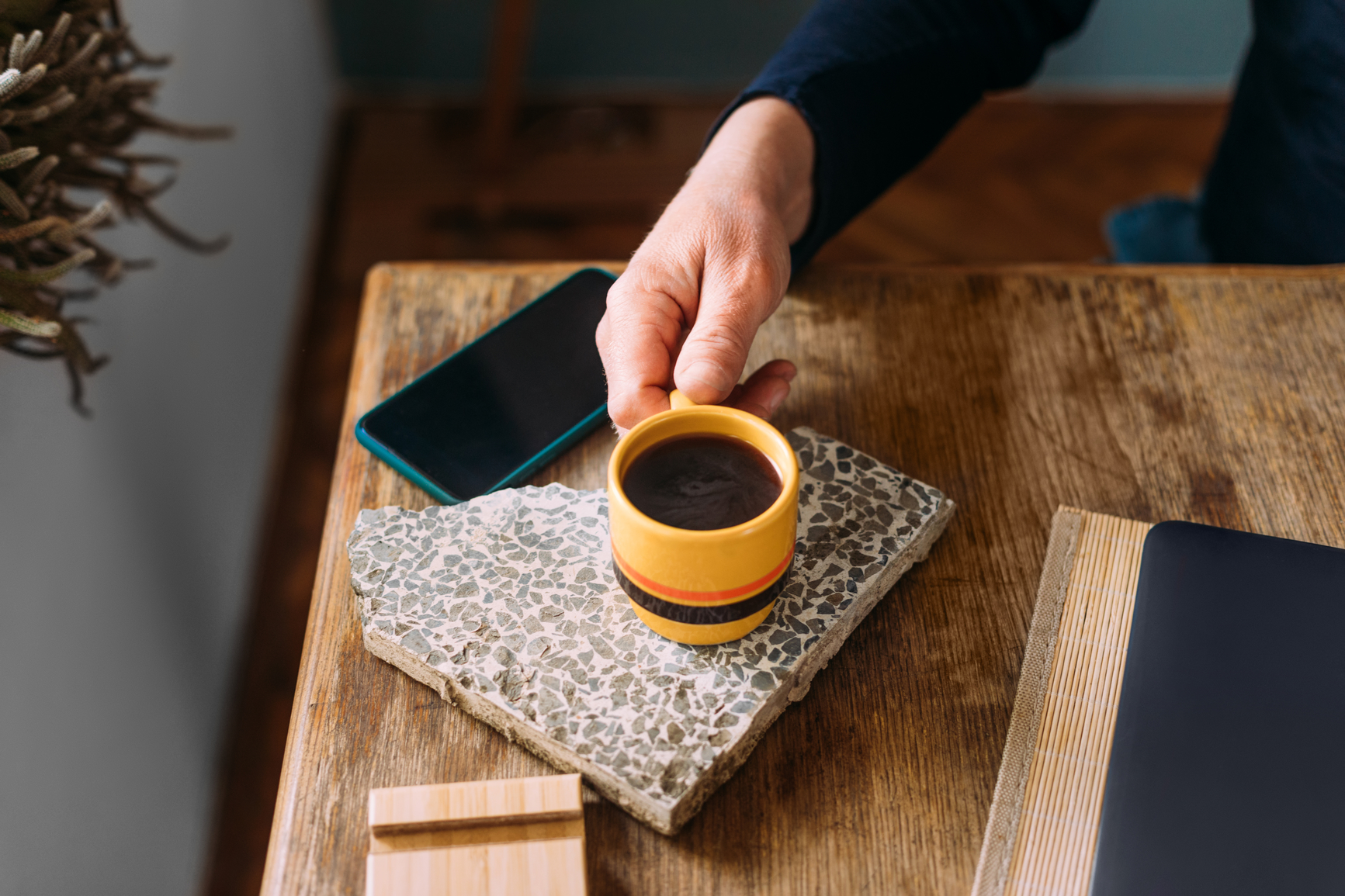 hand taking yellow coffee cup that is placed on the gray slate on the table